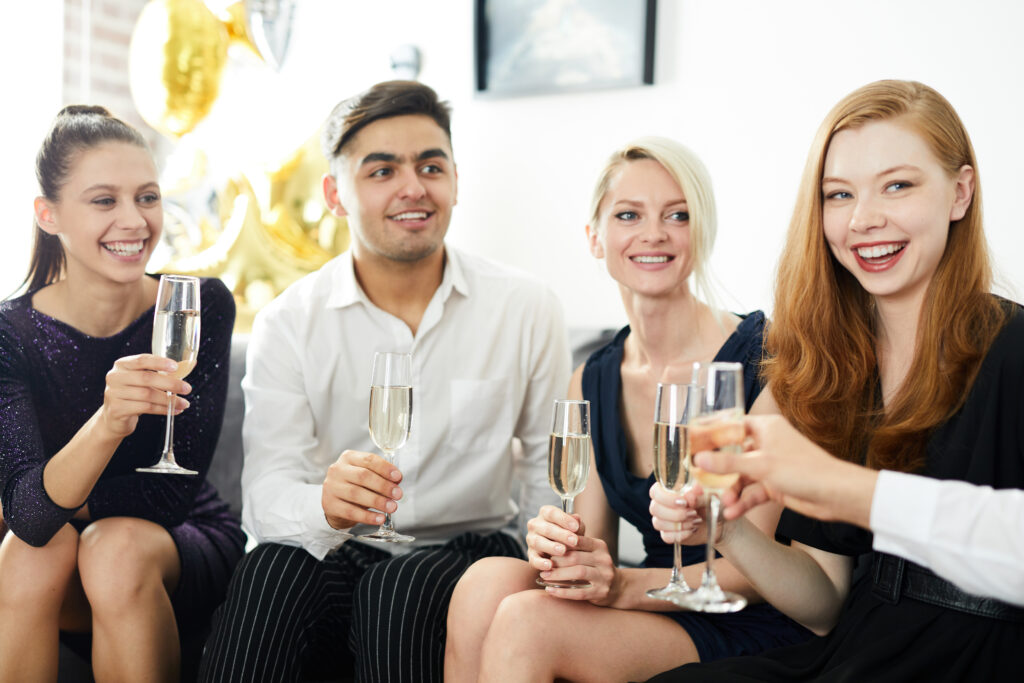Happy guy and three pretty girls in elegant dresses celebrating occasion with champagne