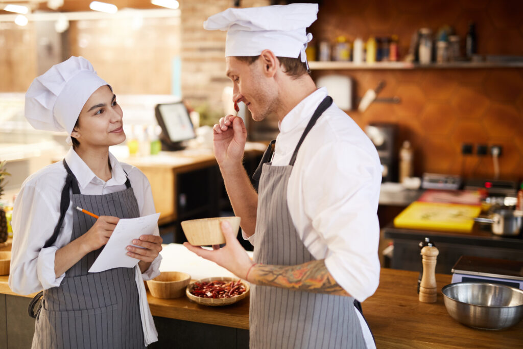 Side view portrait of two professional chefs discussing dishes while cooking in restaurant, copy space